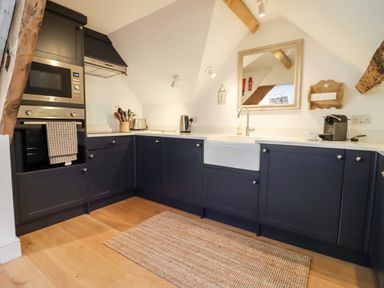 A kitchen with dark blue cabinets wooden floor and a rug at Spring Cottage in Stroud