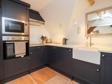 A kitchen with dark cabinets a microwave oven a kettle a toaster utensils and a farmhouse sink at Spring Cottage in Stroud