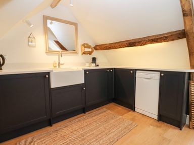 A kitchen with dark cabinets a white sink dishwasher and wooden beams at Spring Cottage in Stroud