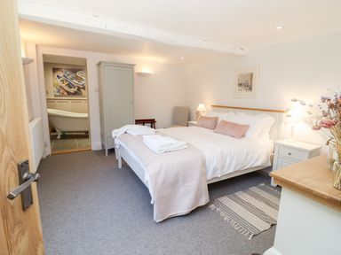 A bedroom with a bed towels on the bed wardrobe and view into a bathroom with a bathtub at Spring Cottage in Stroud