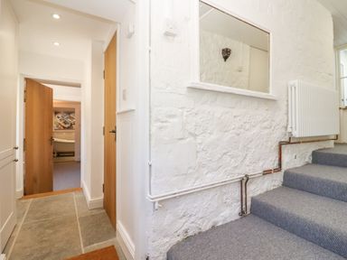 A hallway with stone tile floor leading to a room with an open wooden door and carpeted stairs with a radiator on a white textured wall at Spring Cottage in Stroud