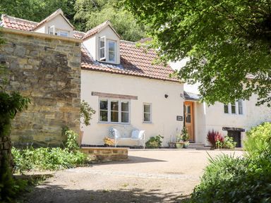 Exterior view of a cottage with a tiled roof a white bench plants and a wooden door at Spring Cottage in Stroud