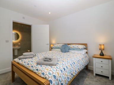 A bedroom with a wooden bed a patterned bedspread towels on the bed a bedside table with a lamp and a door leading to a bathroom at Hedd in Amlwch