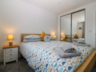 A bedroom with a bed covered in patterned bedding two bedside tables with lamps and mirrored sliding closet doors at Hedd in Amlwch