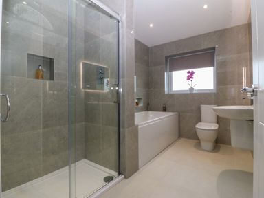 A bathroom with a glass shower enclosure bathtub toilet and sink with a window and a plant on the windowsill at Hedd in Amlwch