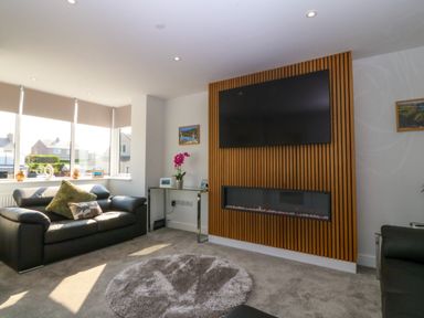 A living room with a black sofa a round rug a wall-mounted TV and a fireplace at Hedd in Amlwch