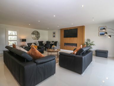 A living room with black leather sofas and a wall-mounted television above a fireplace at Hedd in Amlwch