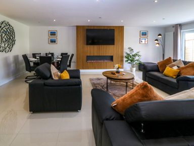 A living room with black sofas pillows a round wooden coffee table and a dining table with chairs at Hedd in Amlwch