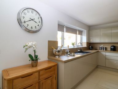 A kitchen with a wooden sideboard and a wall clock above it a countertop with a sink and kitchen appliances at Hedd in Amlwch