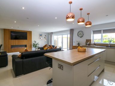 A kitchen and living room with a wooden island three pendant lights and a black sofa at Hedd in Amlwch