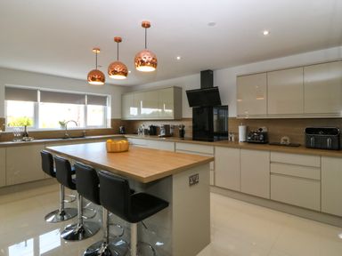 A kitchen with an island with stools appliances and pendant lights at Hedd in Amlwch