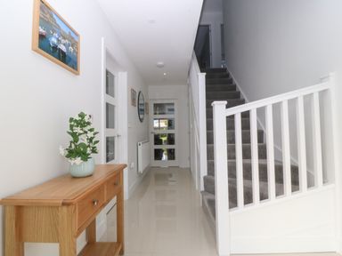 A hallway with stairs carpeted in gray a wooden table with a vase of flowers and doors along the wall at Hedd in Amlwch