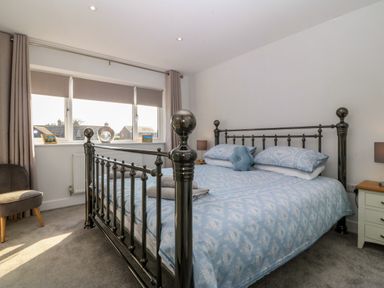 A bedroom with a metal bed frame and blue bedding next to a window with gray curtains at Hedd in Amlwch