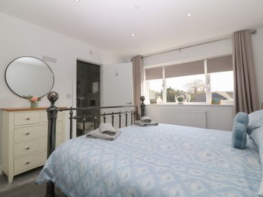 A bedroom with a metal bed frame a chest of drawers with a round mirror and an open door to a bathroom at Hedd in Amlwch