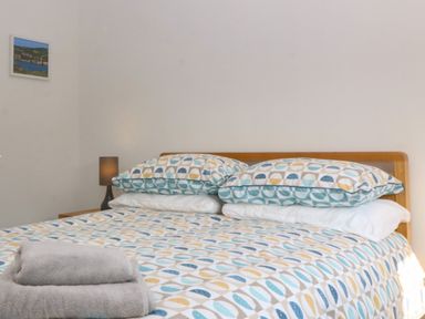 A bed with patterned bedding and two folded towels on top next to a nightstand with a lamp and a small framed picture on the wall at Hedd in Amlwch