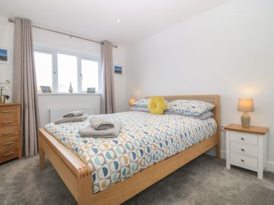 A bedroom with a wooden bed, patterned bedding, bedside tables with lamps, a dresser and curtains at Hedd in Amlwch