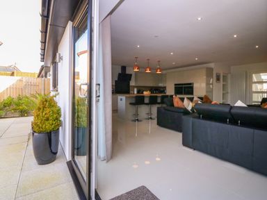 An open living room and kitchen area with black sofas and bar stools at Hedd in Amlwch