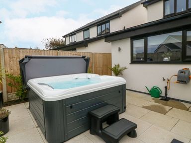 A hot tub with steps in a paved outdoor area next to a house with a window and wooden fence at Hedd in Amlwch