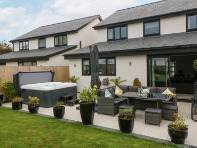 A backyard patio with a hot tub and outdoor seating area at Hedd in Amlwch