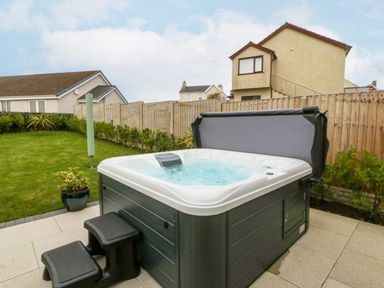 A hot tub with steps in a backyard with a wooden fence and houses at Hedd in Amlwch