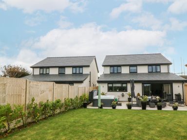 A backyard with grass lawn wooden fences potted plants seating area and two modern houses in Hedd Amlwch