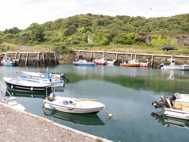 A small harbor with several moored motorboats and a stone wall with green hills in the background at Hedd in Amlwch