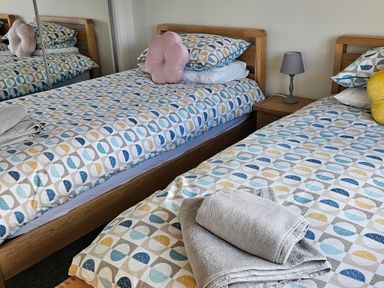 A bedroom with two single beds with patterned bedding bedside table with lamp and folded towels at Hedd in Amlwch