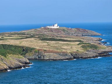 A coastal landscape with a building on a hill overlooking the sea at Hedd in Amlwch