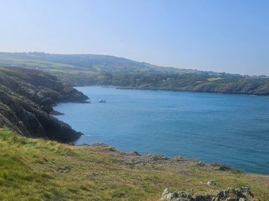 A coastal landscape with rocky cliffs grass and a boat on the water at Hedd in Amlwch