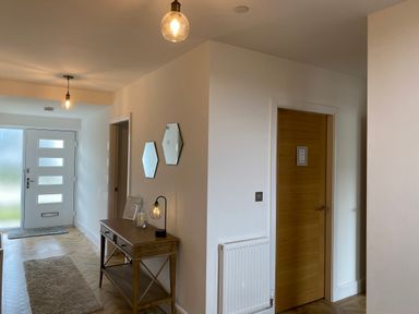 An entrance hallway with a wooden console table two hexagonal mirrors rugs wooden doors and hanging light fixtures at Galwad y Mor in Broad Haven