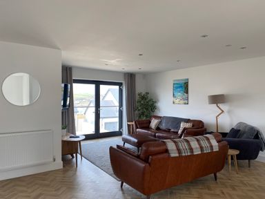A living room with brown leather sofas a gray armchair a wooden floor a round mirror and large glass doors at Galwad y Mor in Broad Haven