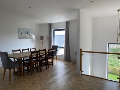 A dining room with a wooden table surrounded by chairs and a large window with curtains at Galwad y Mor in Broad Haven