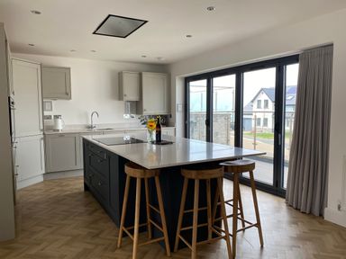 A kitchen with a central island and three wooden stools near large glass doors at Galwad y Mor in Broad Haven
