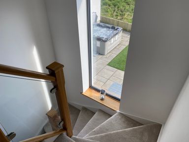 A stairway with wooden and glass railing next to a window showing a hot tub outside at Galwad y Mor in Broad Haven