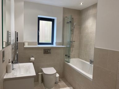 A bathroom with a bathtub shower combination a toilet sink and a window at Galwad y Mor in Broad Haven