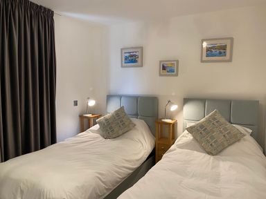 A bedroom with two single beds with bedside tables with lamps and framed pictures on walls at Galwad y Mor in Broad Haven