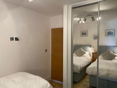A bedroom with white bedding a wooden door mirrored wardrobe and framed pictures on the wall at Galwad y Mor in Broad Haven