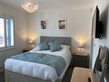 A bedroom with a bed two bedside tables lamps a television and a window at Galwad y Mor in Broad Haven