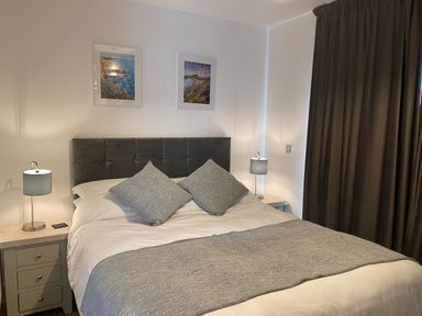 A bedroom with a double bed two bedside tables with lamps and two framed pictures on the wall at Galwad y Mor in Broad Haven