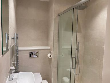 A bathroom with a sink and faucet a toilet with a chrome flush panel a glass shower enclosure with a rainfall showerhead and handheld showerhead at Galwad y Mor in Broad Haven