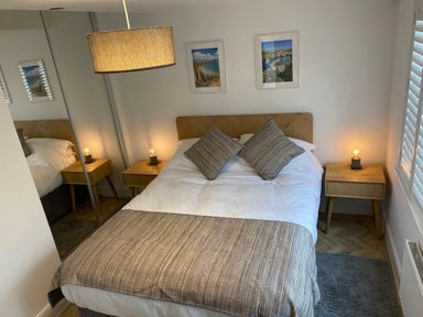 A bedroom with a double bed between two wooden bedside tables with lamps and pictures on the wall at Galwad y Mor in Broad Haven