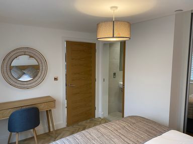 A bedroom with wooden doors a round mirror above a wooden desk a blue chair and a bed with a textured blanket at Galwad y Mor in Broad Haven