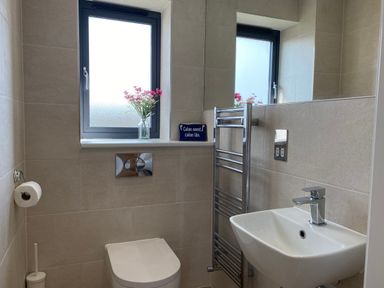 A bathroom with a toilet sink towel rack and a window with flowers on the sill at Galwad y Mor in Broad Haven