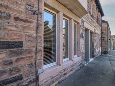 Stone exterior wall with three windows and a doorway along a paved street at Glencoe House in Wooler