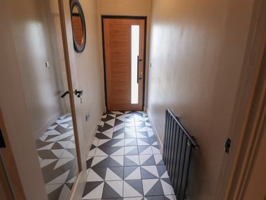 A hallway with geometric patterned floor tiles a wooden front door a black radiator and a round mirror at Glencoe House in Wooler
