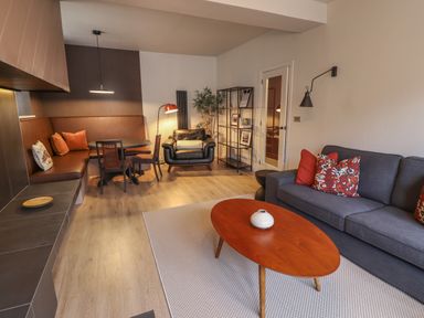 A living room with a gray sofa red cushions a wooden coffee table and a dining area with brown seating at Glencoe House in Wooler