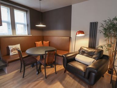 A dining area with a round table two chairs a brown corner bench and a black armchair with a cushion and a floor lamp next to a plant at Glencoe House in Wooler
