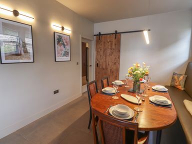 A dining room with a wooden table set for six people with plates glasses and a flower vase at Glencoe House in Wooler