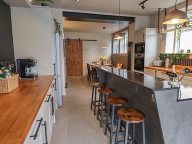 A kitchen with a long island with stools a wooden countertop appliances and a dining area with a wooden door at Glencoe House in Wooler