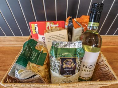 A basket with a bottle of white wine, tea bags, biscuits, and pasta on a wooden surface at Glencoe House in Wooler